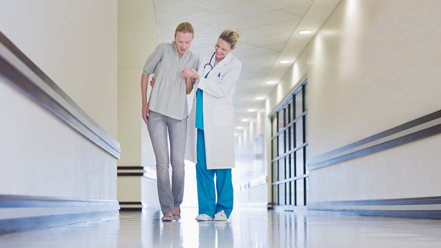 female doctor helping female patient walk down hallway