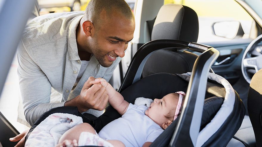 Father leans into rear of car to smile at baby in car seat