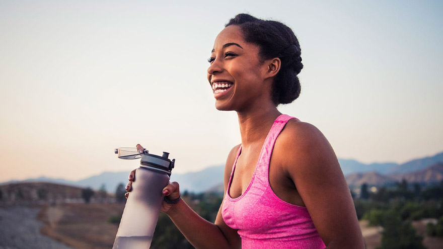 Woman on trail smiling holding water bottle
