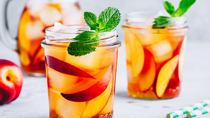 Homemade peach mocktail with fresh mint and ice cubes in glass jar on gray stone background.