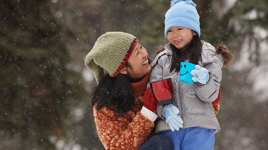 Chinese mother hugging daughter in the snow and drinking hot chocolate