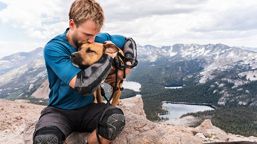 Man kissing dog while sitting on mountain against cloudy sky