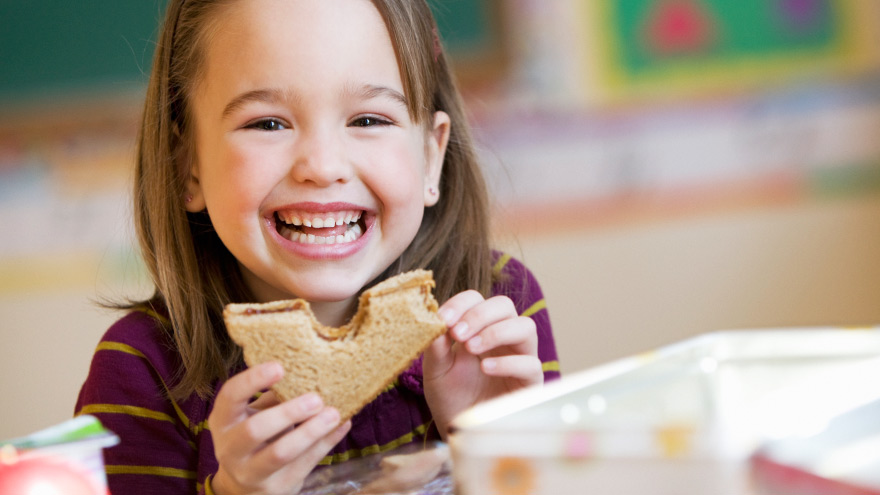 A child smiling and holding a sandwich 