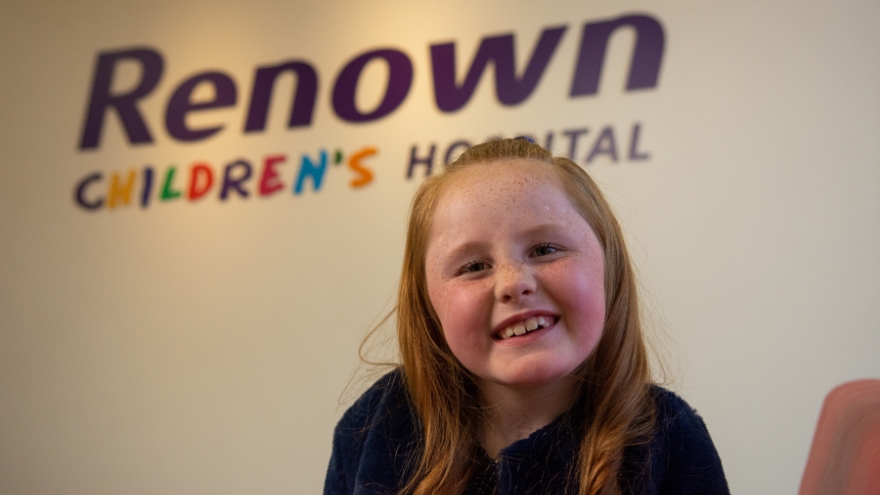Children's Miracle Network Champion Child Shaylie Edwards smiles for the camera in front of the Renown Children's Hospital logo.